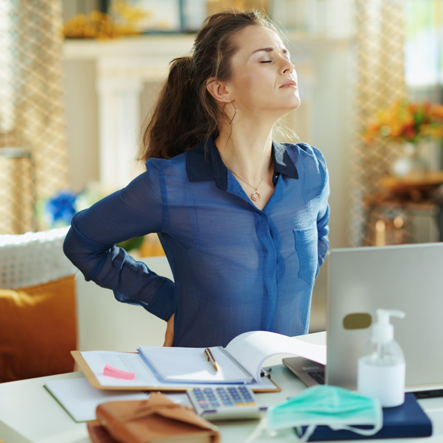 Woman-sitting-at-desk-holding-back-in-pain